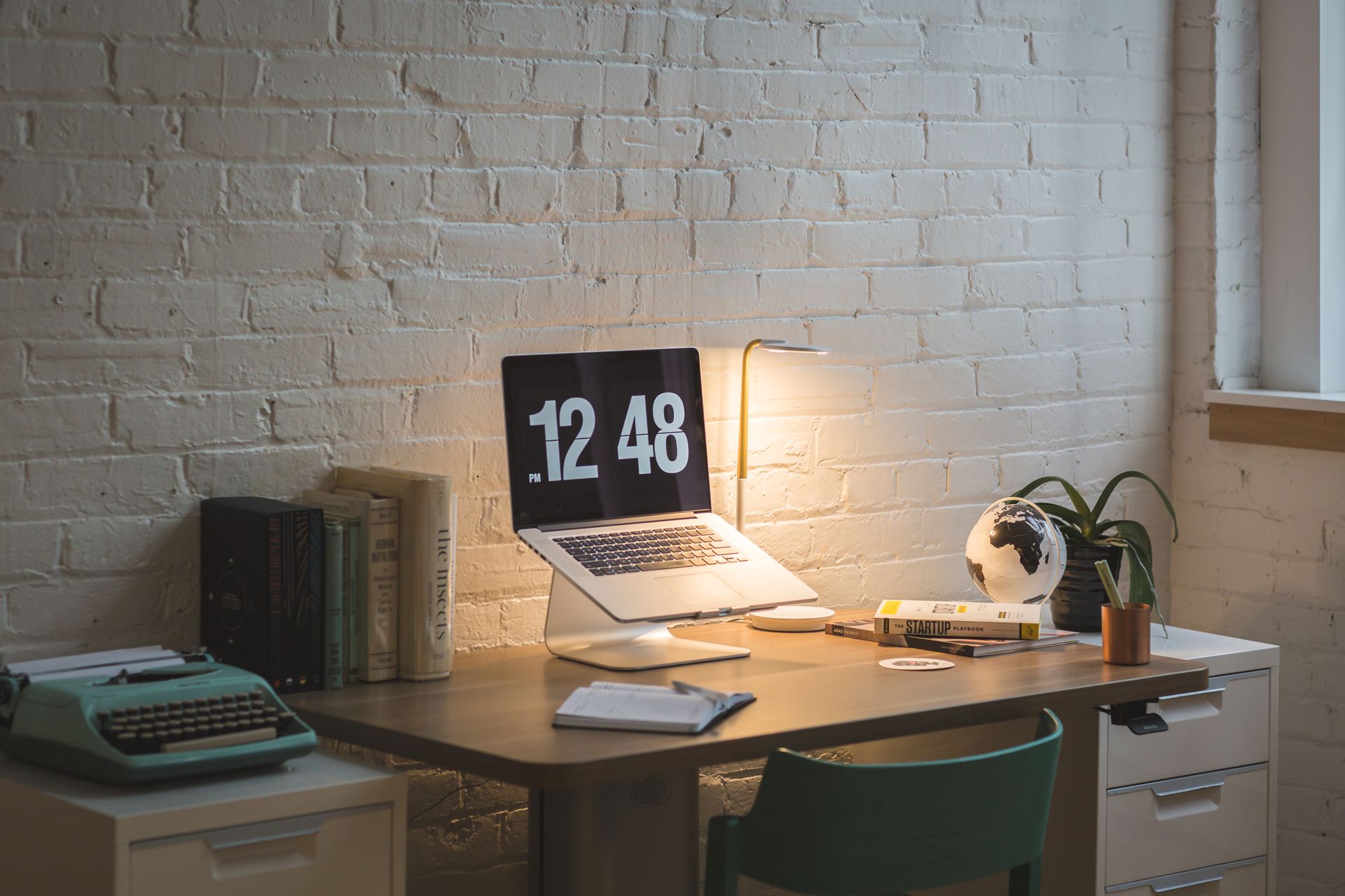 Schreibtisch mit Laptop und Lampe vor einer Backsteinwand